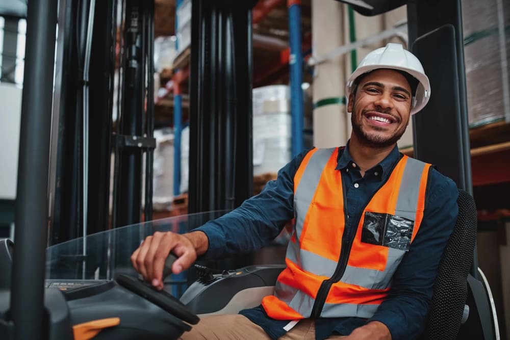 a smiling forklift driver wearing a safety vest and hardhat