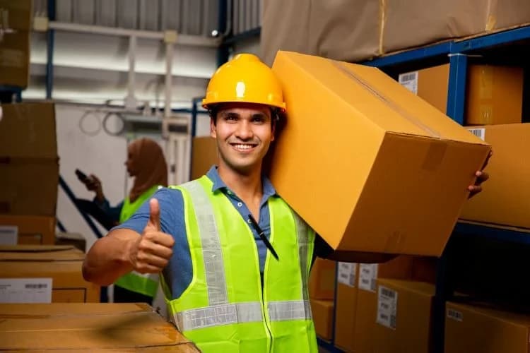 a warehouse worker holding a box on his shoulders and giving a thumbs up